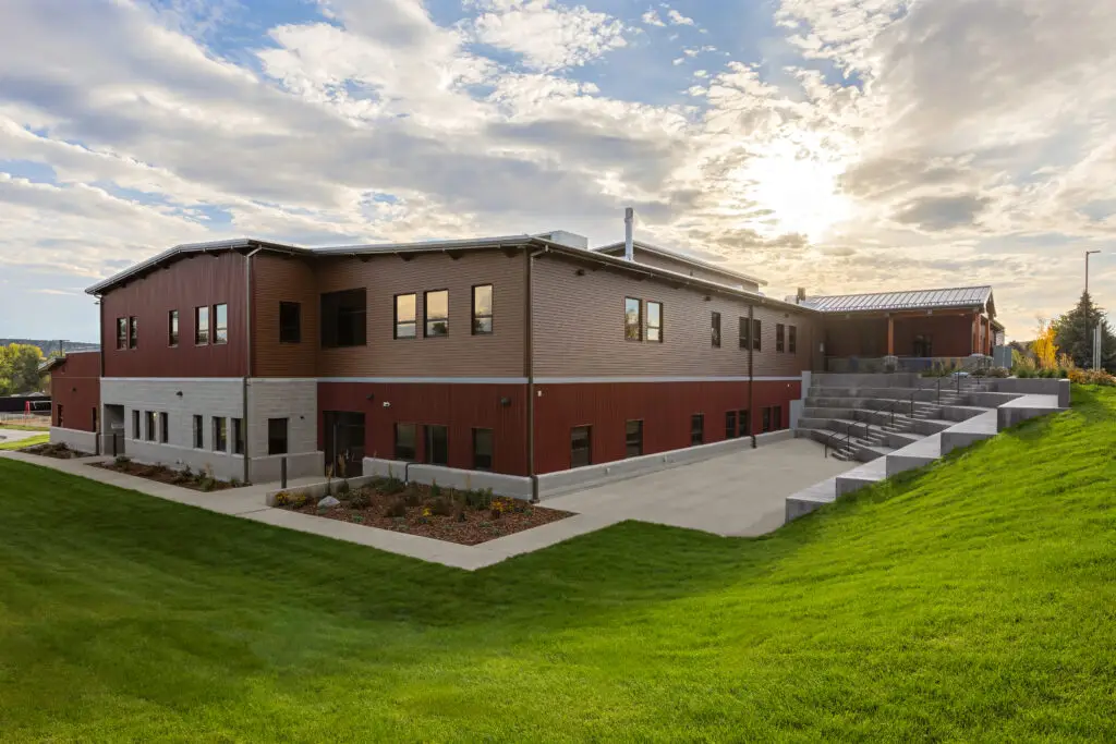 Back exterior of the school featuring metal siding, tiered concrete seating, walkways, and landscaped green space, completed by Groathouse Construction.