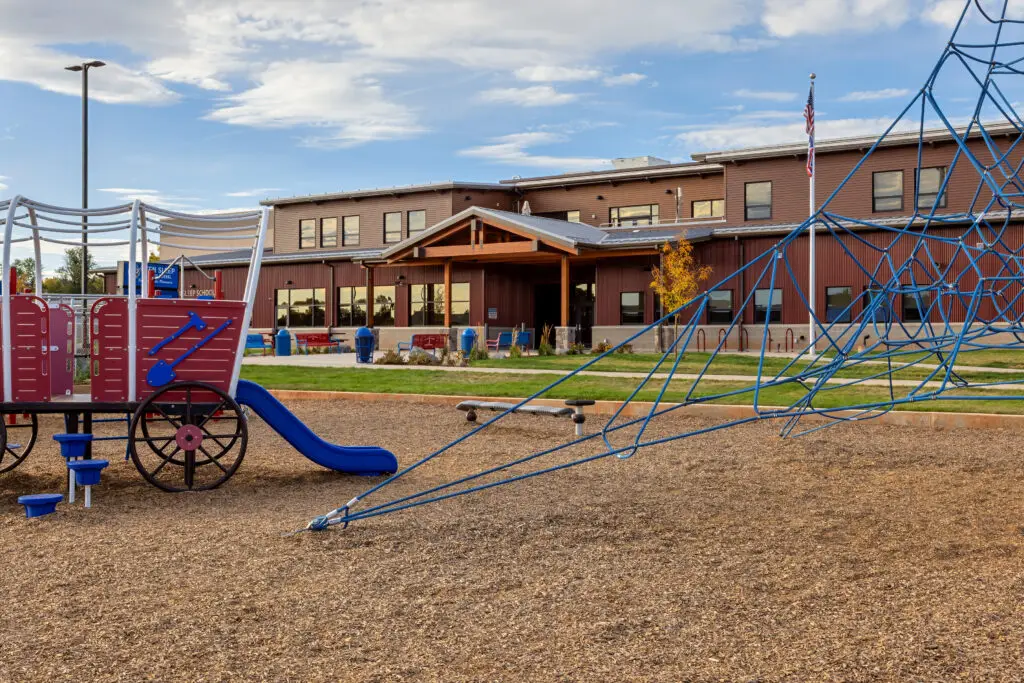 School playground with climbing structures and slide in front of the main school building constructed by Groathouse Construction.
